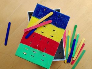 Geschenkidee für zweijährige Jungs. DIY Farbsortierspiel aus einem Karton und farbigen Holzstäbchen.